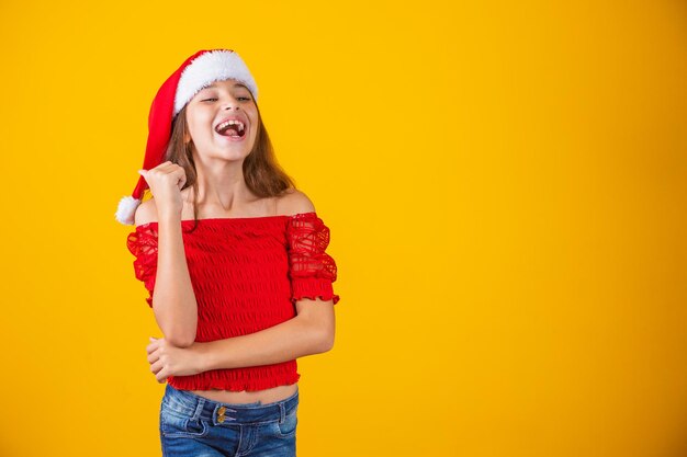 Klein meisje gekleed voor Kerstmis wijzend met haar duim op vrije ruimte voor tekst. Eindejaarspromotie en campagnes