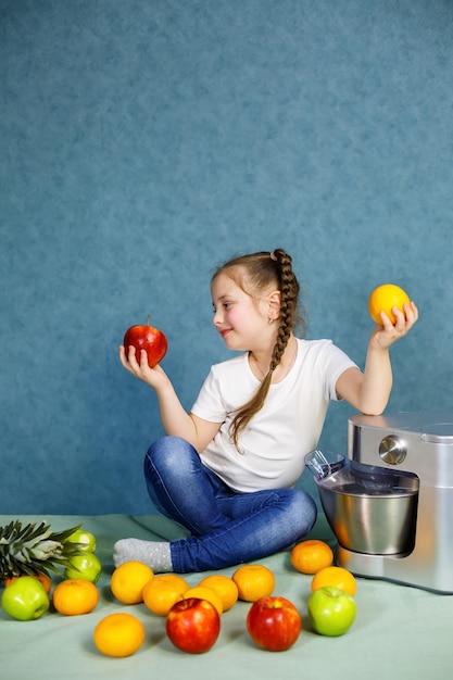 Klein meisje geperst vers sap van fruit van appels en sinaasappel. Vitaminen en gezonde voeding voor kinderen.