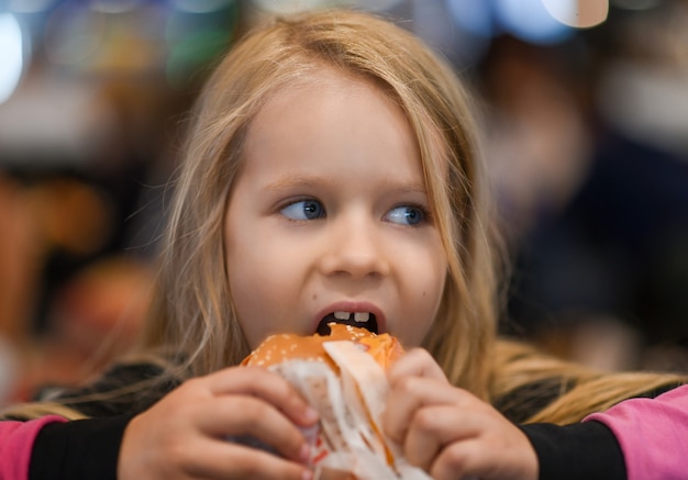 Klein meisje hamburger eten in fastfood café.