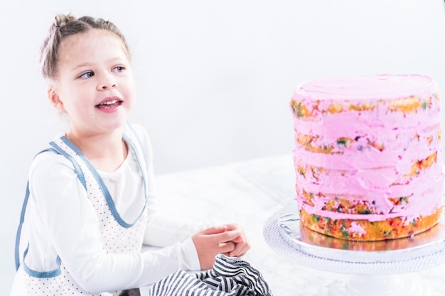 Klein meisje helpt bij het bakken van hoge funfetti cake met roze botercrème glazuur