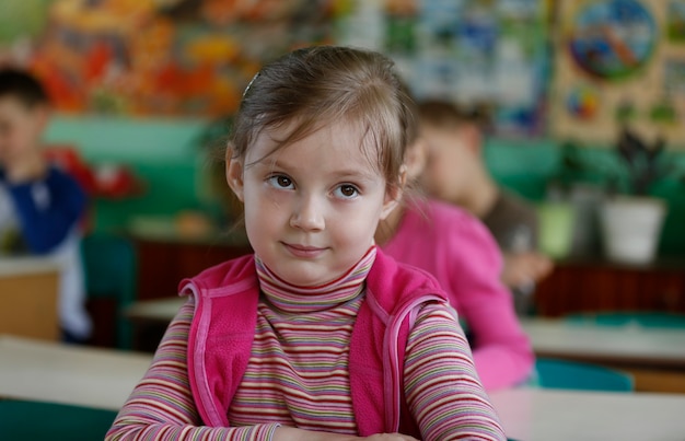 Klein meisje, het kind zit in de kleuterschool aan de tafel, glimlachend. Pre-school girl