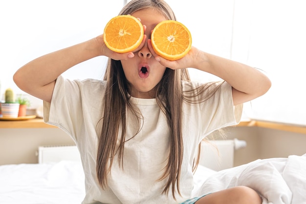 Klein meisje houdt sinaasappels bij haar ogen terwijl ze in bed zit