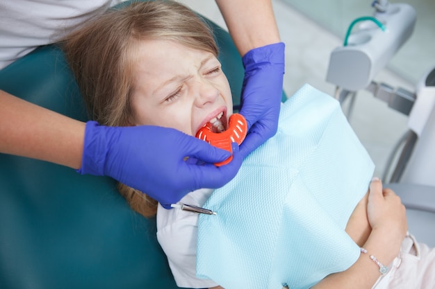 Klein meisje huilt in tandartsstoel terwijl tandarts tandheelkundige afdrukken maakt met stopverf