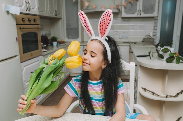 Klein meisje in de keuken in konijnenoren met een boeket tulpen paastraditie