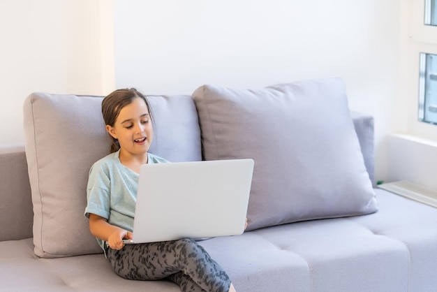 Klein meisje in de leerplichtige leeftijd studeert thuis. een meisje kijkt naar een videoles op een laptopmonitor en schrijft taken in een notitieboekje.
