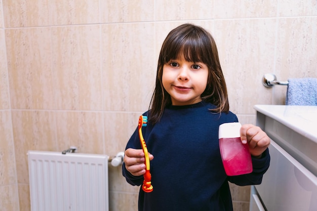 Klein meisje in donkerblauw sweatshirt, glimlachend, met borstel haar tandenborstel en tandpasta, in de badkamer. Tandenpoetsen, hygiëne en kindertijd concept.