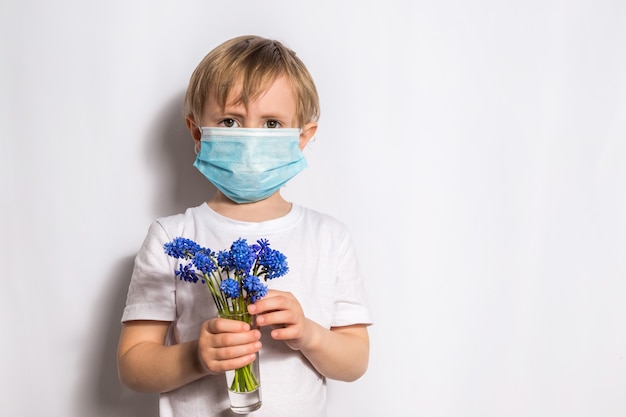 Klein meisje in een beschermend medisch masker houdt een glas met blauwe bloemen