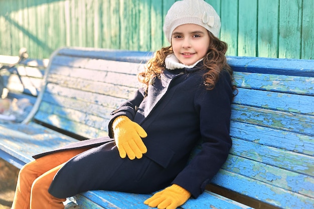 Klein meisje in een blauwe jas op een bankje in het najaar. Hoge kwaliteit foto