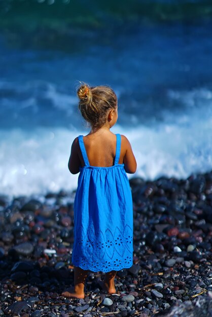 Klein meisje in een blauwe jurk spelen op het strand van Paradisos in Santorini