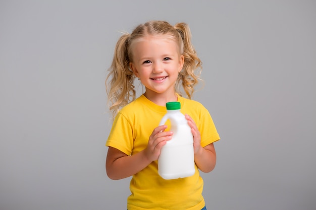 klein meisje in een geel t-shirt met plastic flessen melk