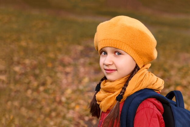 Klein meisje in een gele baret op een achtergrond van herfstopen plek met gevallen bladeren
