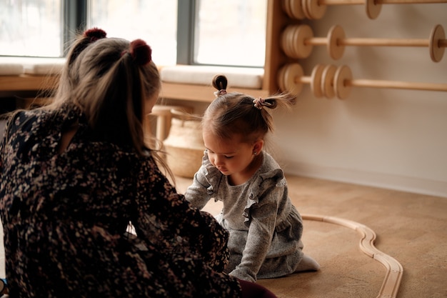 Klein meisje in een grijze jurk speelt in de kinderkamer met een houten spoorweg en een trein die hij is