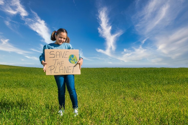 Klein meisje in een groen veld met een blauwe lucht, met een kartonnen bord waarop staat: RED DE PLANEET.