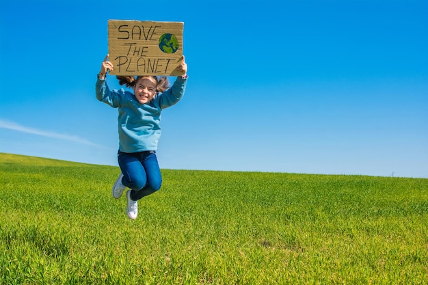 Klein meisje in een groen veld met een blauwe lucht, met een kartonnen bord waarop staat: RED DE PLANEET.
