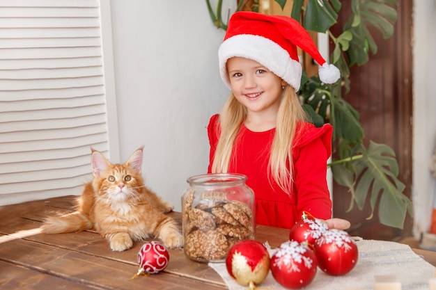 klein meisje in een kerstmuts met een kat in de keuken