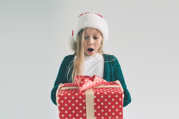 Klein meisje in een kerstmuts met geschenken op witte achtergrond