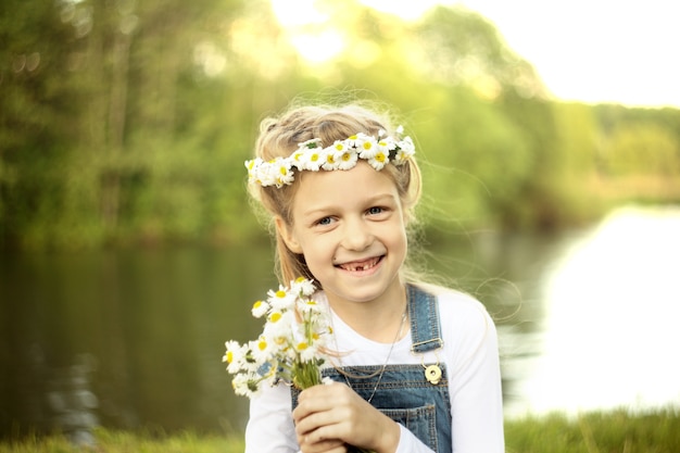 Klein meisje in een krans van madeliefjes en een boeket bloemen in het park op een zonnige dag