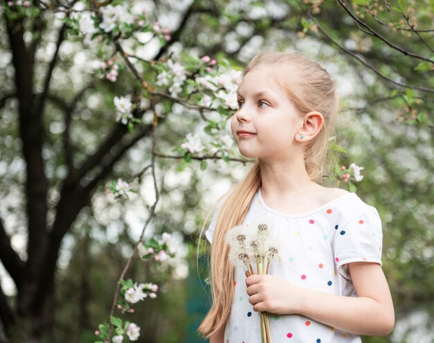 Klein meisje in een lentetuin met witte paardebloemen in haar handen