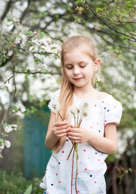 Klein meisje in een lentetuin met witte paardebloemen in haar handen