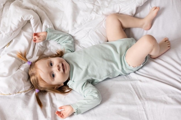 klein meisje in een lichtgroene bodysuit ligt in bed gemaakt met wit beddengoed Hoge kwaliteit foto