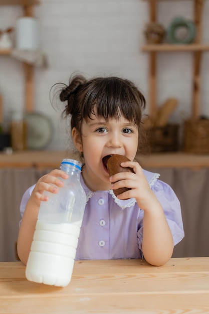 klein meisje in een lila jurk drinkt melk en eet een broodje aan de keukentafel. ruimte voor tekst, banner