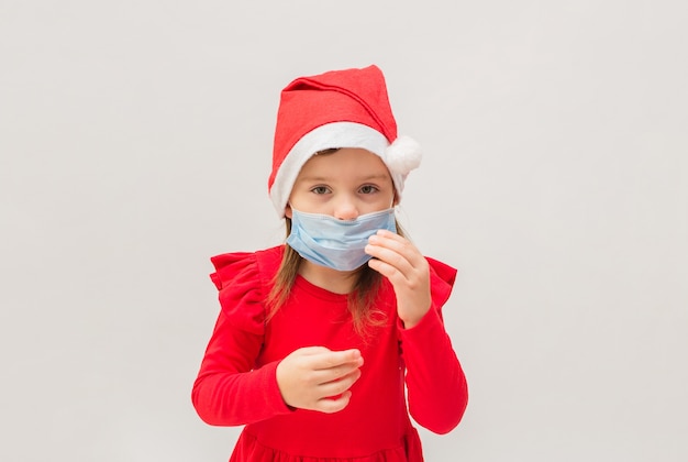 Klein meisje in een medisch masker in een rode dop op een witte muur met ruimte voor tekst