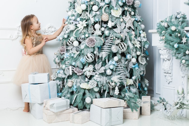 Klein meisje in een mooie jurk hangt decoraties aan de kerstboom.