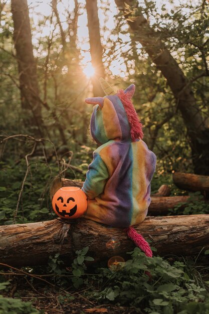 Foto klein meisje in een regenboog eenhoorn kostuum kigurumi zit met haar rug naar de camera