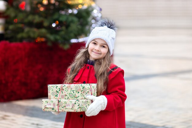 Klein meisje in een rode jas met kerstcadeaus