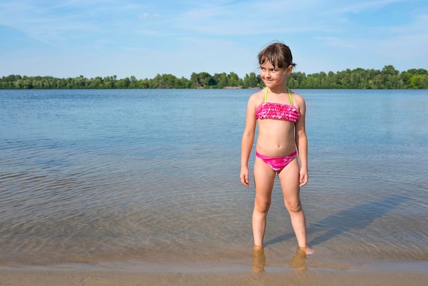 Klein meisje in een roze badpak op de rivier op een zonnige warme dag