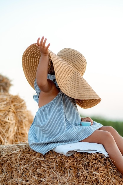 Klein meisje in een veld met hooirollen bij zonsondergang Landschap van een veld met hooibergen stro bij zonsondergang Een klein meisje in een blauwe jurk staat midden in een weiland Harmonie en liefde voor de natuur