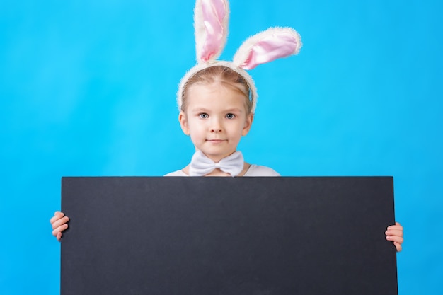 Klein meisje in een wit konijn kostuum met lege bordje of poster