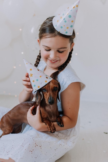 Klein meisje in een witte jurk met haar geliefde hond teckel in haar armen viert haar verjaardag