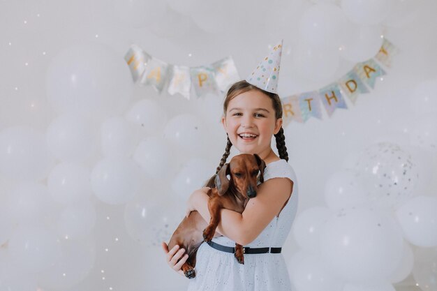 Klein meisje in een witte jurk met haar geliefde hond teckel in haar armen viert haar verjaardag