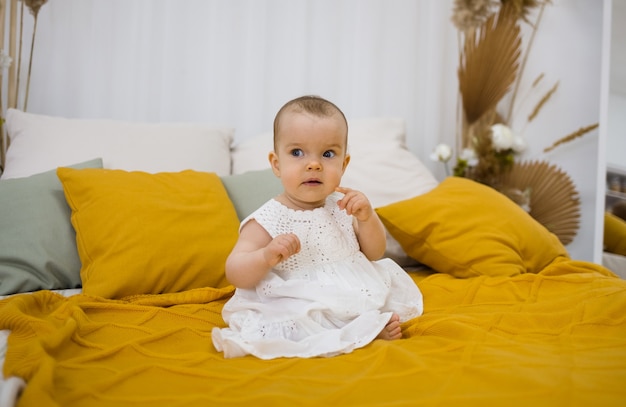 Klein meisje in een witte jurk zit op een gele deken op een bed met ruimte voor tekst