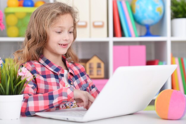 Klein meisje in geruit overhemd met moderne laptop in haar kamer