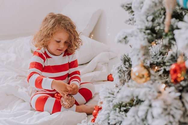 Klein meisje in gestreepte kerstpyjama's siert de kerstboom. levensstijl. hoge kwaliteit foto