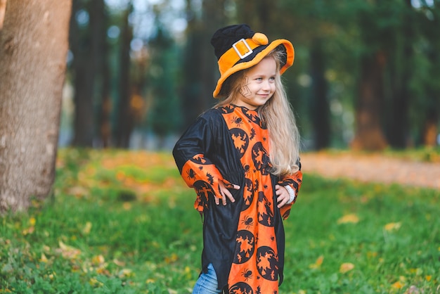 Klein meisje in heksenkostuum staat in het park in de herfst op Halloween-vakantie.