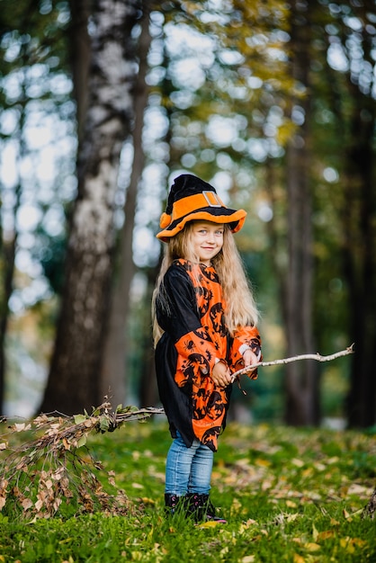 Klein meisje in heksenkostuum vliegt op een bezemsteel in het park voor de Halloween-vakantie.