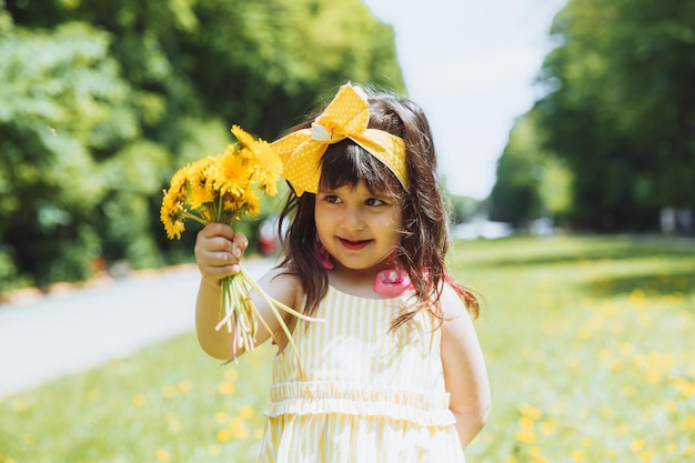 Klein meisje in het park dat gele paardebloembloemen plukt op een zonnige zomerdag