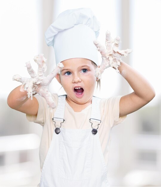 Foto klein meisje in hoed en schort koken in de keuken