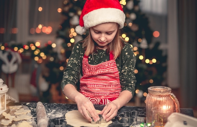 Klein meisje in kerstmuts die koekjes snijdt