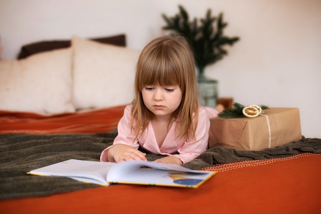 Klein meisje in pyjama met kerstcadeau leesboek in bed
