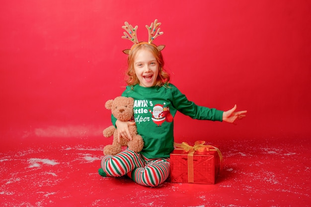 Klein meisje in pyjama op een rode achtergrond met geschenken