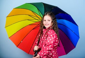 Klein meisje in regenjas regenbescherming regenboog herfst mode vrolijk hipster kind in positieve stemming gelukkig klein meisje met kleurrijke paraplu wachten op inspiratie