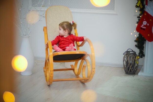 Klein meisje in rode jurk spelen in de kamer met kerstversieringen in een schommelstoel