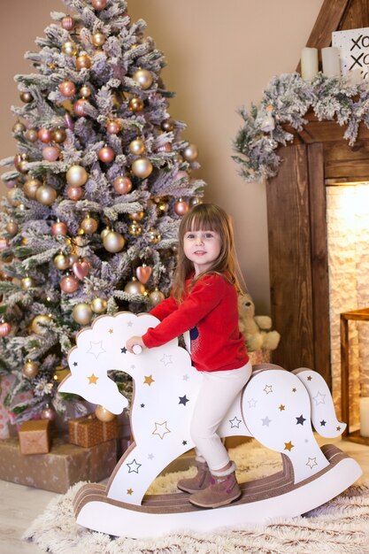 klein meisje in rode pyjama rijdt thuis een houten paard