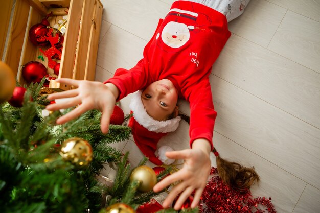 klein meisje in rode pyjama speelt op de vloer onder de kerstboom Nieuwjaarsconcept