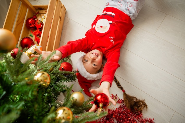 klein meisje in rode pyjama speelt op de vloer onder de kerstboom Nieuwjaarsconcept