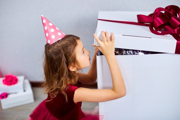 klein meisje in roze jurk en hoed open groot cadeau geschenkdoos met ballonnen thuis verjaardagsfeestje